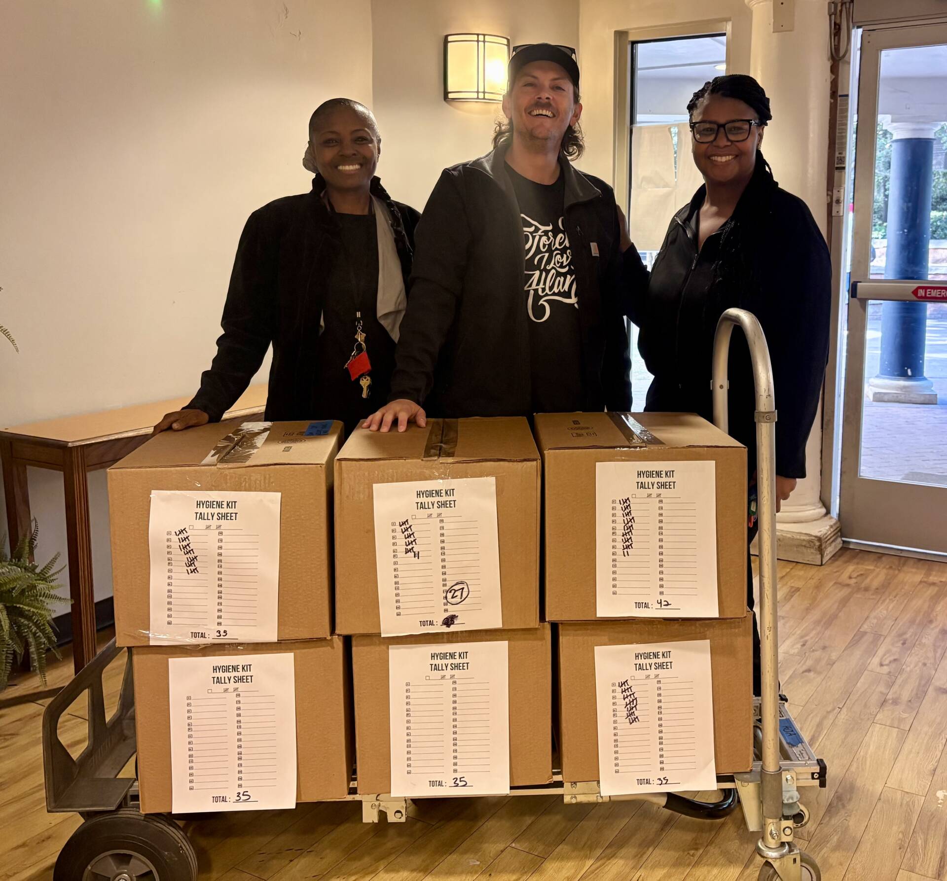 Three 3Keys staff members receive boxes of hygiene kits for residents of Welcome House