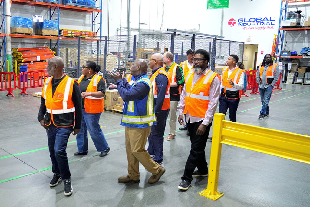 A group of people in safety vests takes a tour of a supply warehouse.