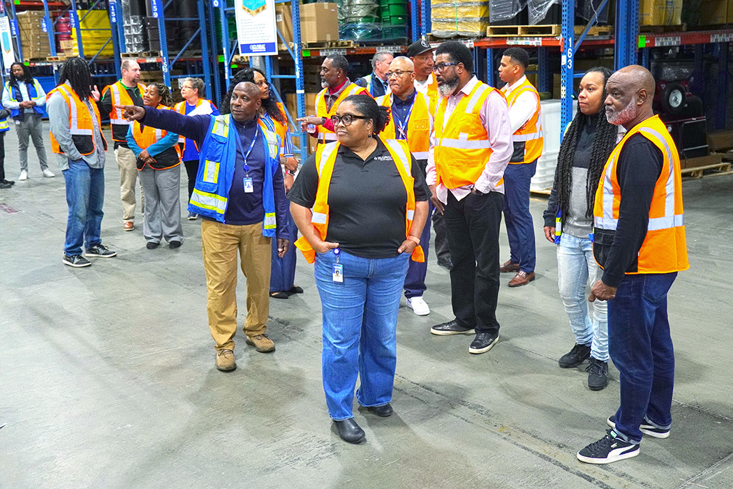 A group of people in safety vests takes a tour of a supply warehouse.