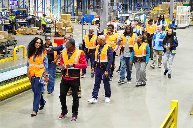 A group of people in safety vests takes a tour of a supply warehouse.