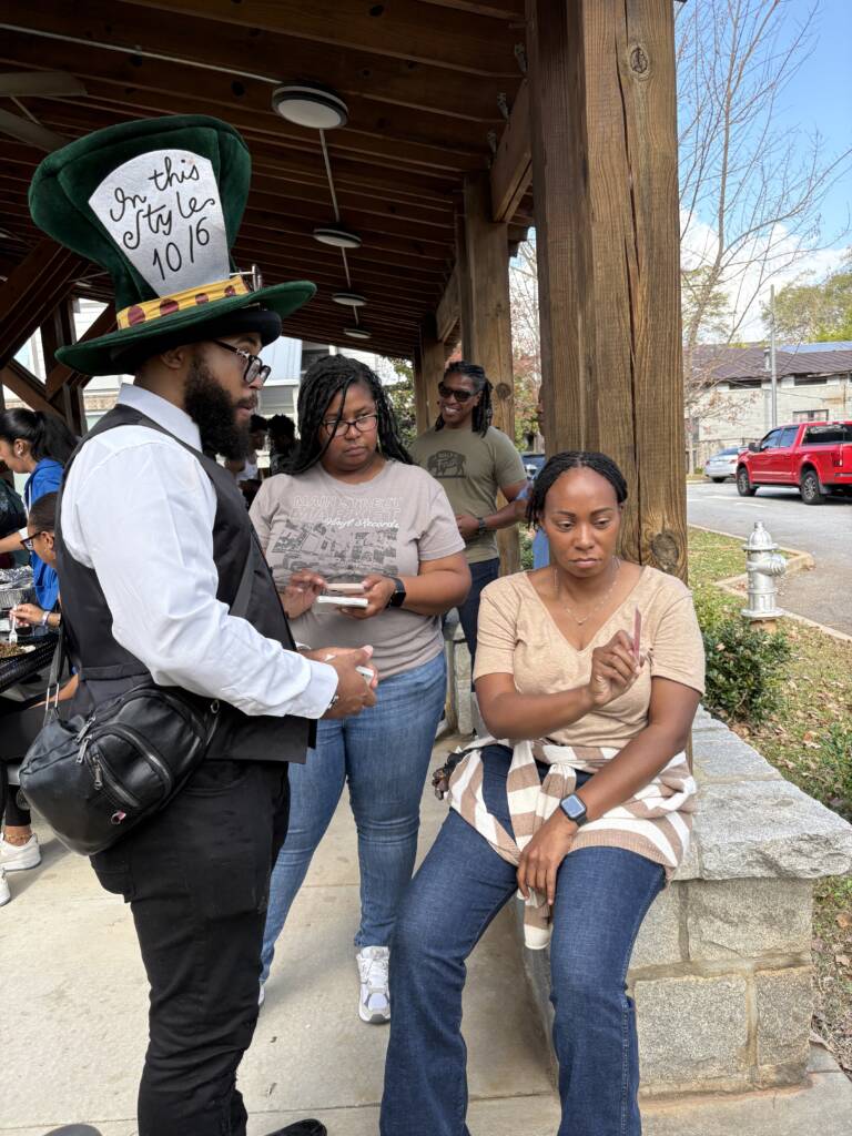 The magician, Lightskini the Lightskin Houdini, performs a trick for an event goer.